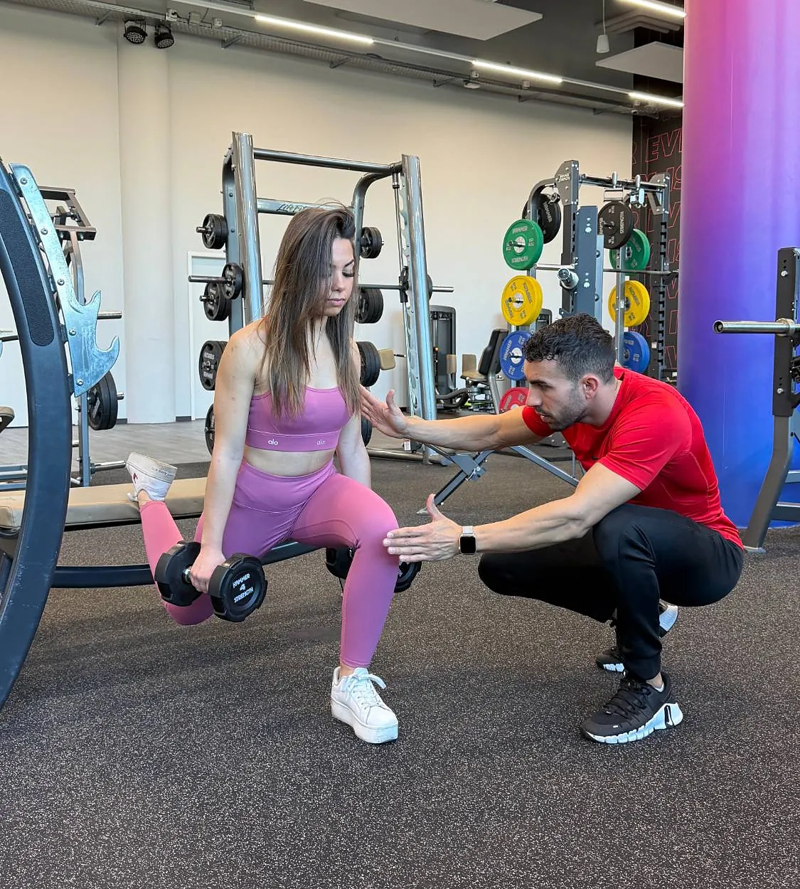 Samy, coach sportif à Genève, corrige la position d’une cliente pendant des fentes bulgares avec haltères