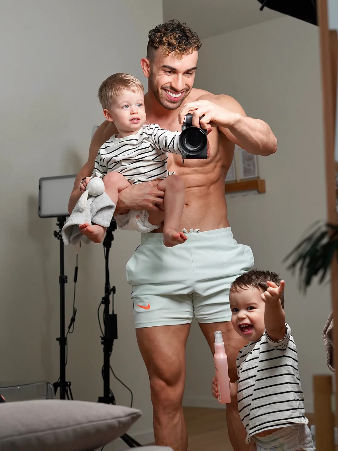 Samy avec ses jumeaux Soan et Sacha, 3 ans : l’un dans son bras, l’autre qui rit à ses pieds, un appareil photo Sony à la main